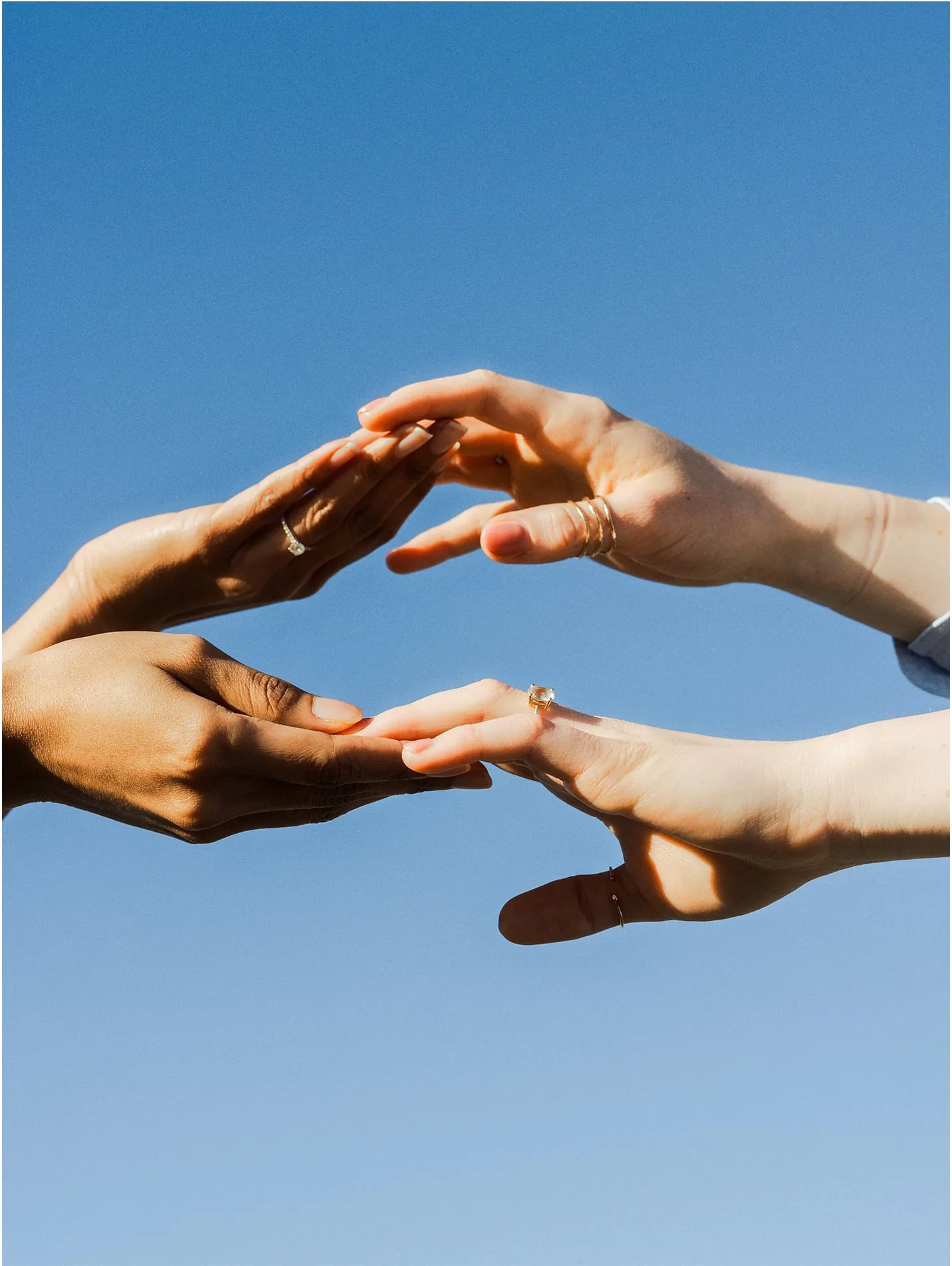 Two hands with rings reaching toward each other against a clear blue sky