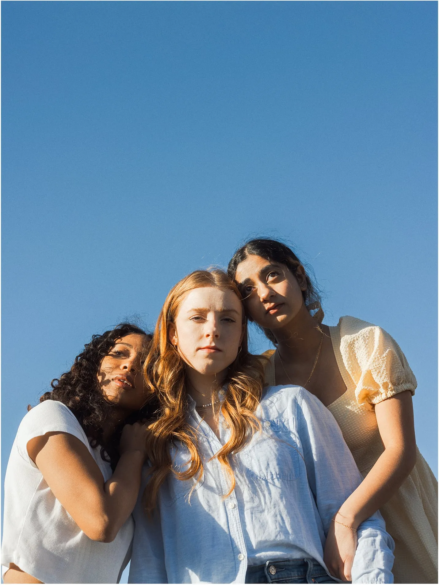 Three friends leaning together in golden light against a blue sky