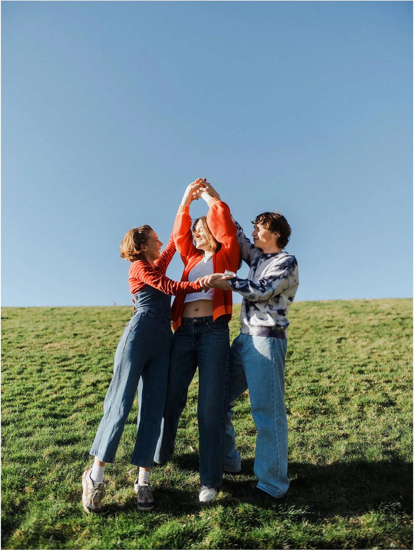 Three friends dancing in a circle on a grassy hill