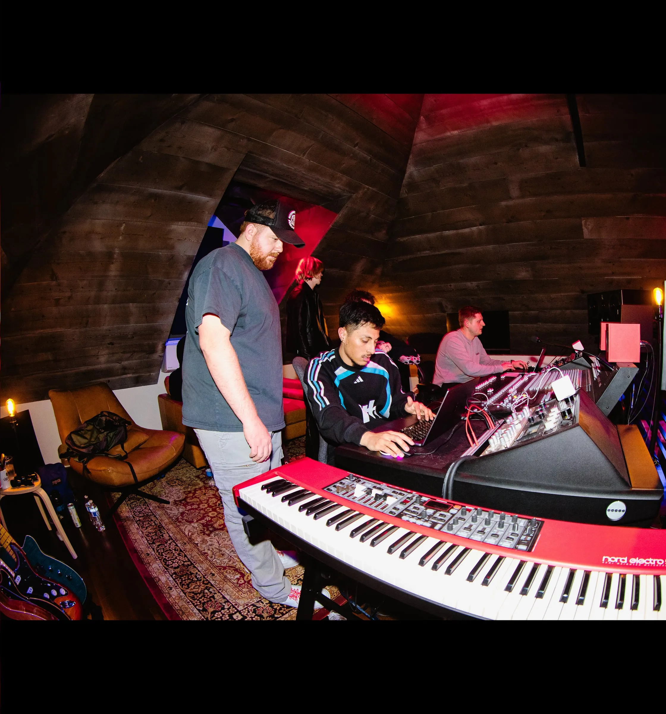 Musicians working over keyboards and a mixing desk in a wood-paneled studio