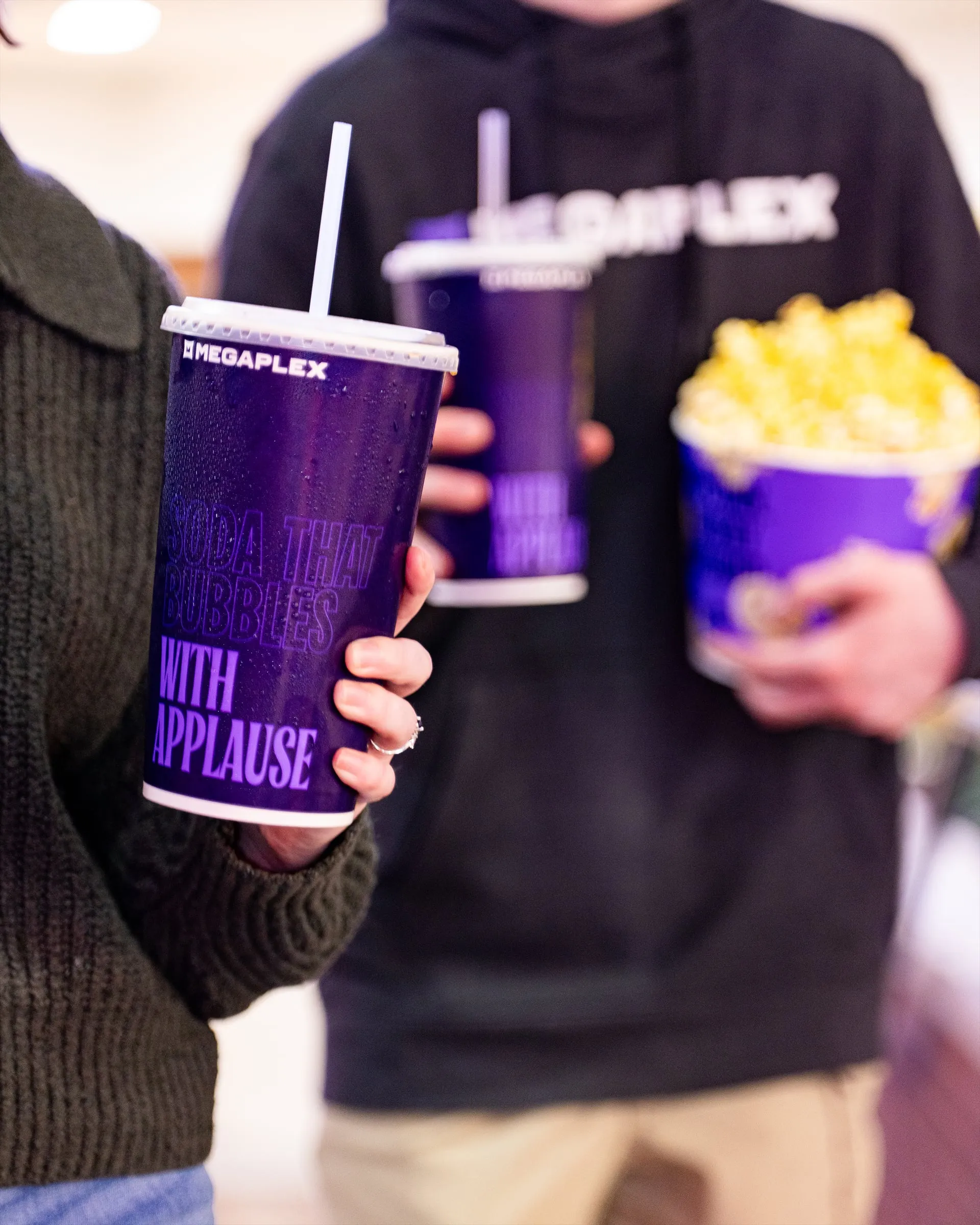 Moviegoers carrying purple sodas and a bucket of popcorn