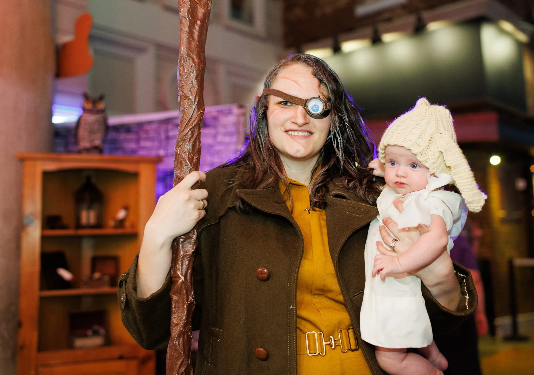 Costumed fan with a staff and eyepatch holding a baby in a knit cap