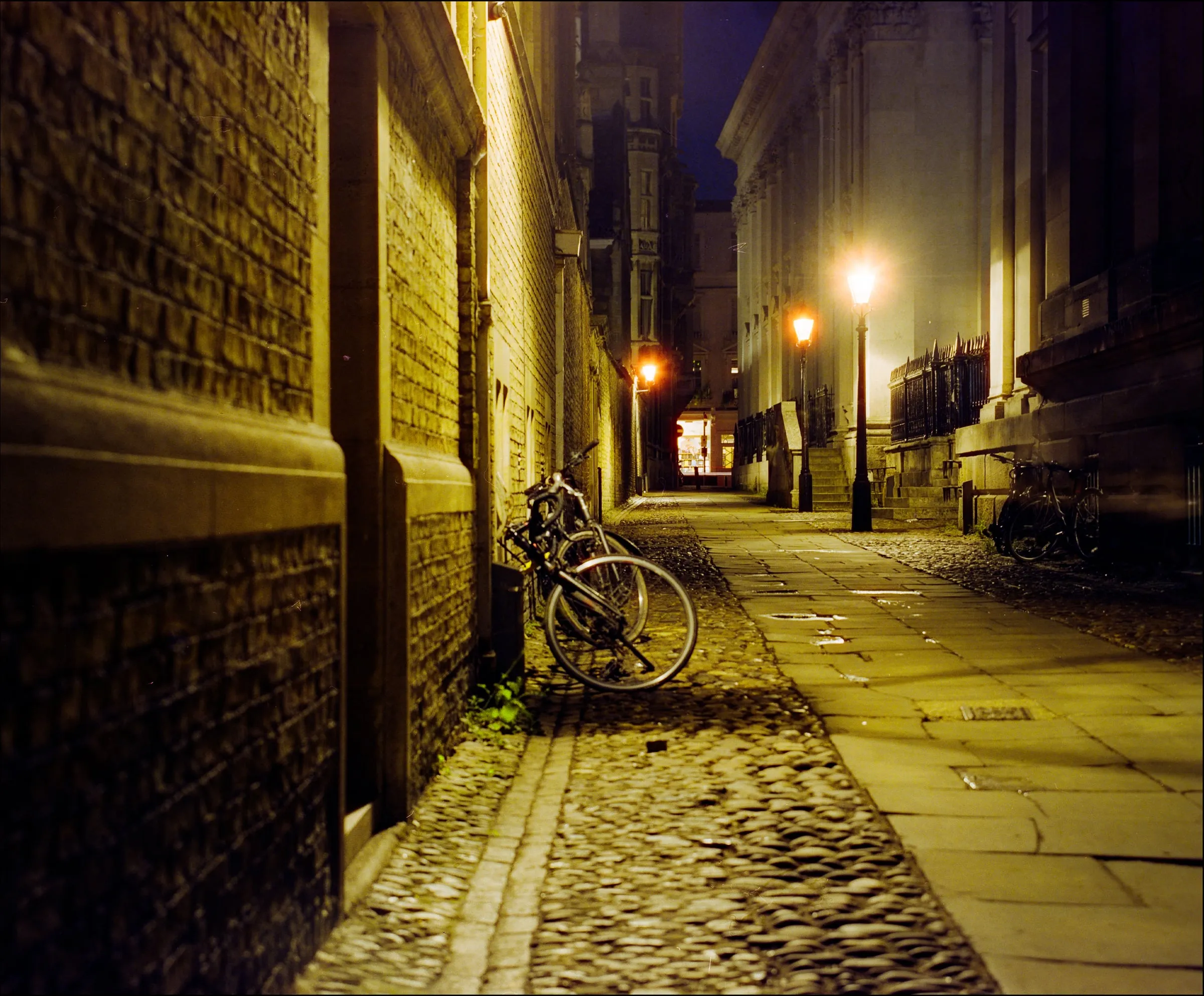 Bicycles leaning against a brick wall in a lamplit cobblestone lane