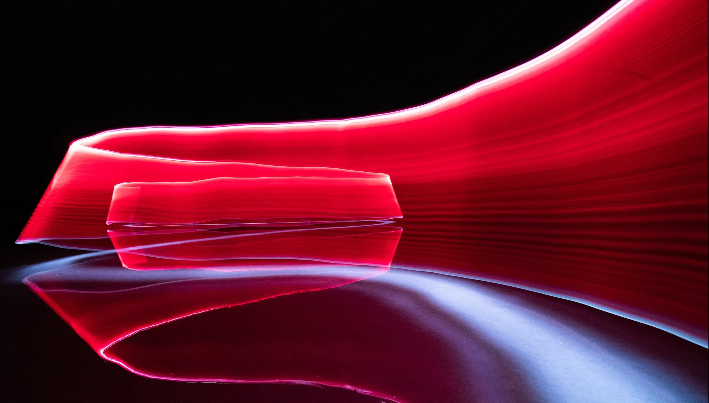 Ribbons of red light folded over a reflective surface in the dark