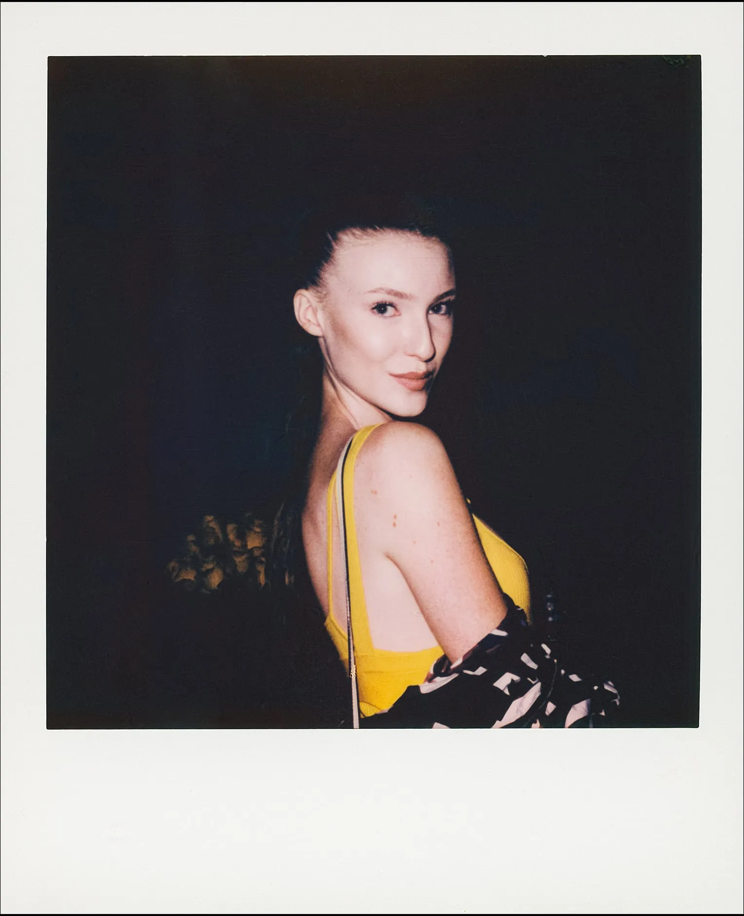 Polaroid portrait of a woman in yellow glancing over her shoulder