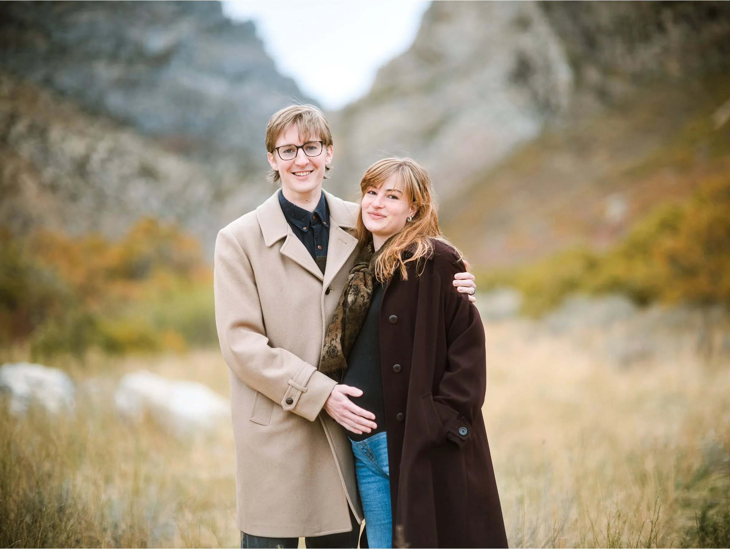 Couple in wool coats embracing in a golden canyon meadow
