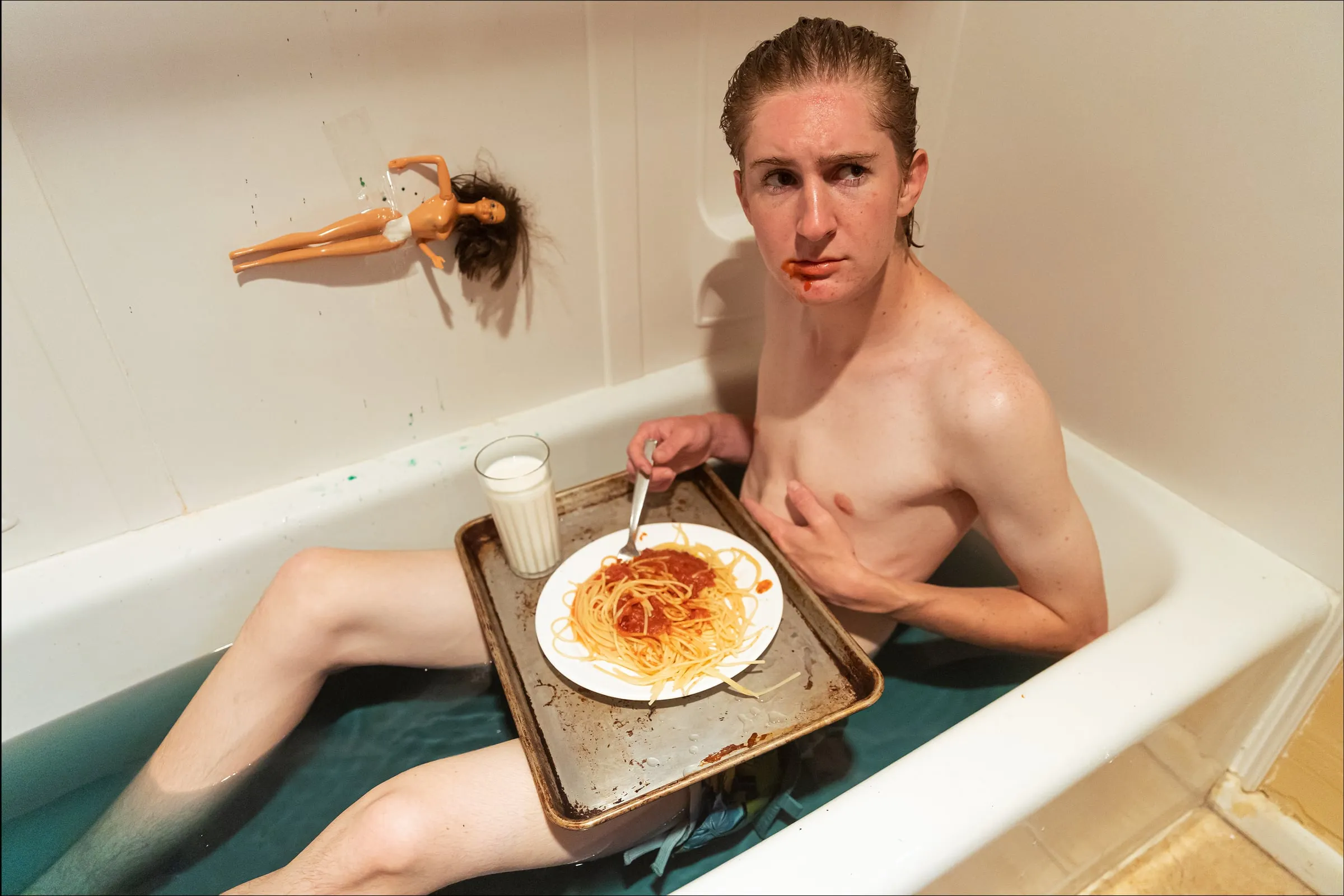 Conceptual portrait of a man eating spaghetti from a tray in a bathtub