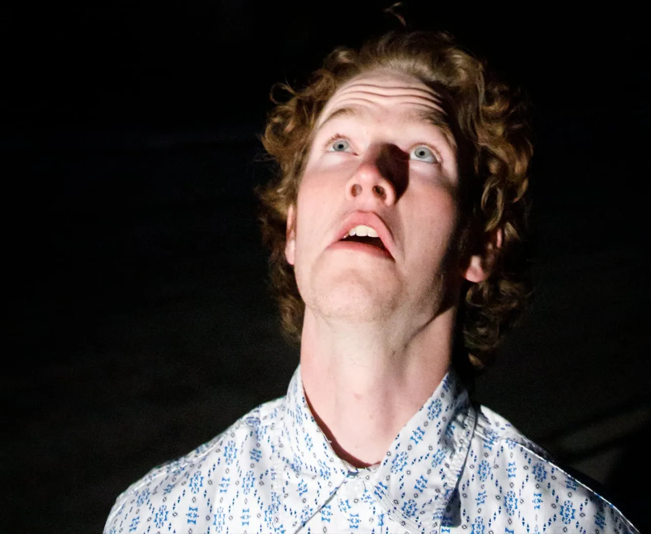 Man lit by a single beam looking up into darkness