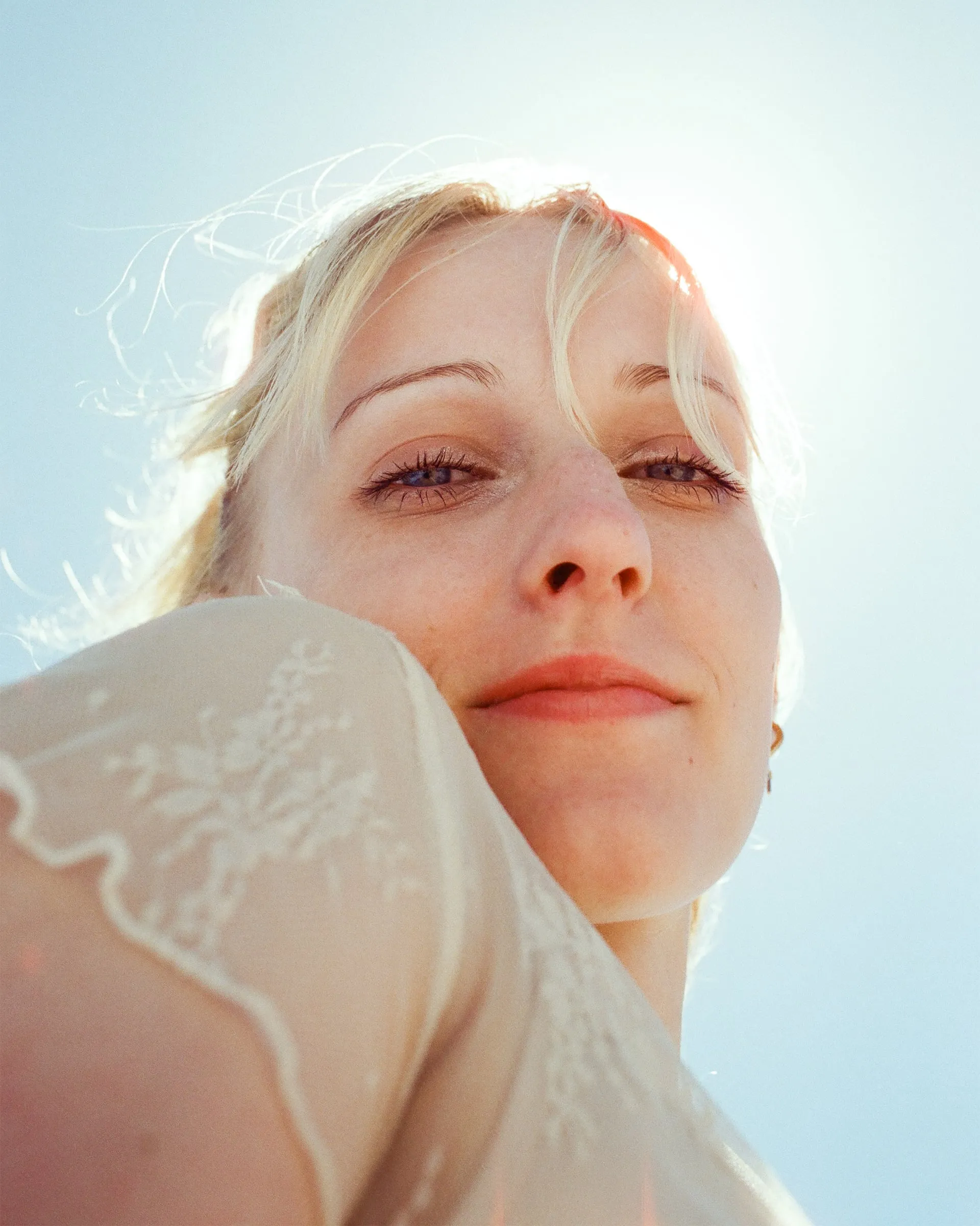 Backlit close-up of a blonde woman in lace smiling into the low sun