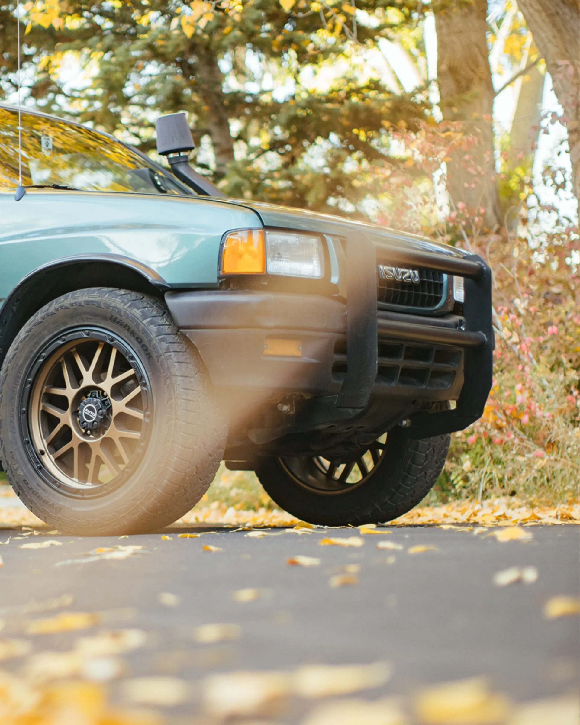 Close front quarter of a lifted Isuzu Rodeo among fallen yellow leaves
