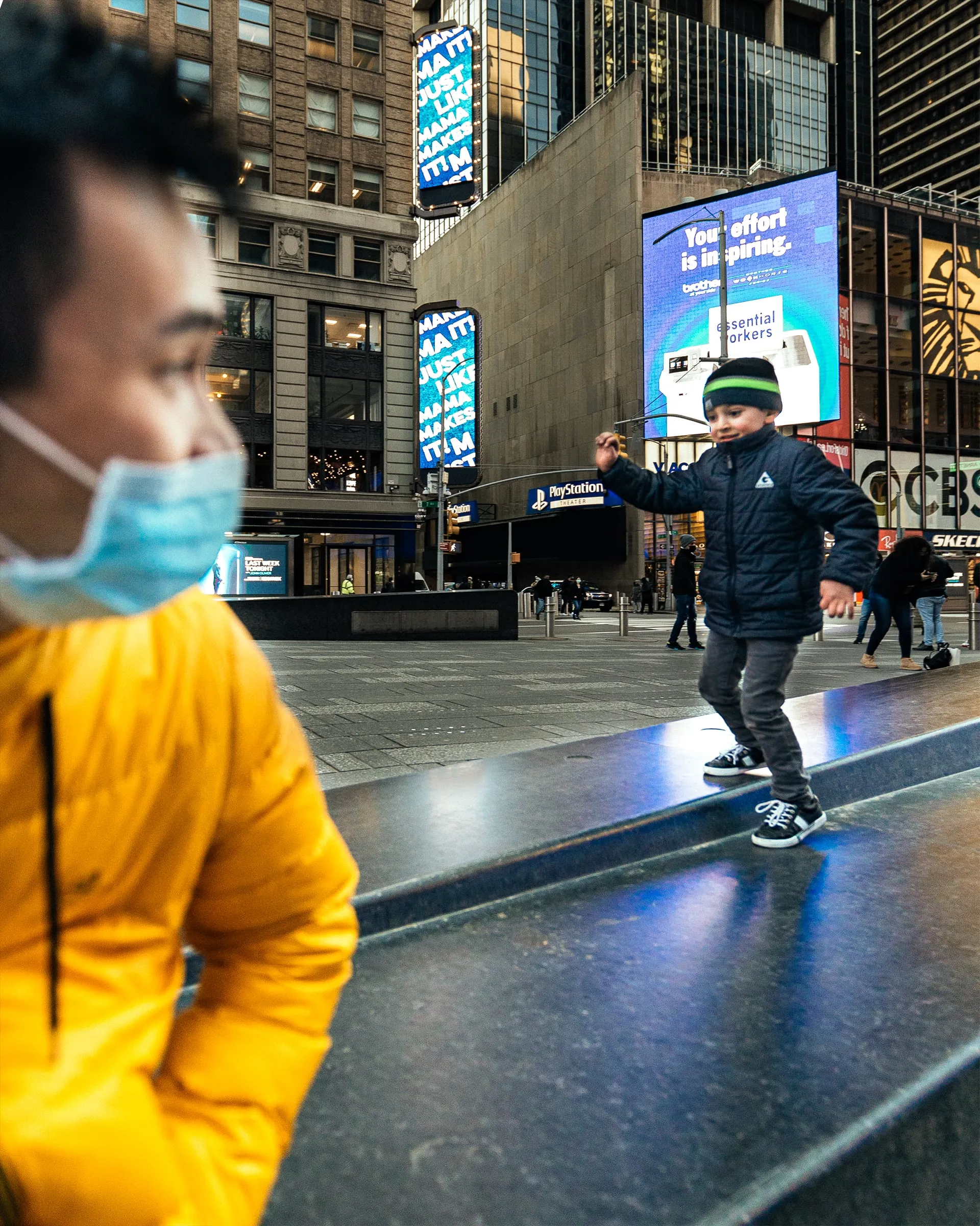 Boy balancing along a granite ledge in Times Square while his father watches