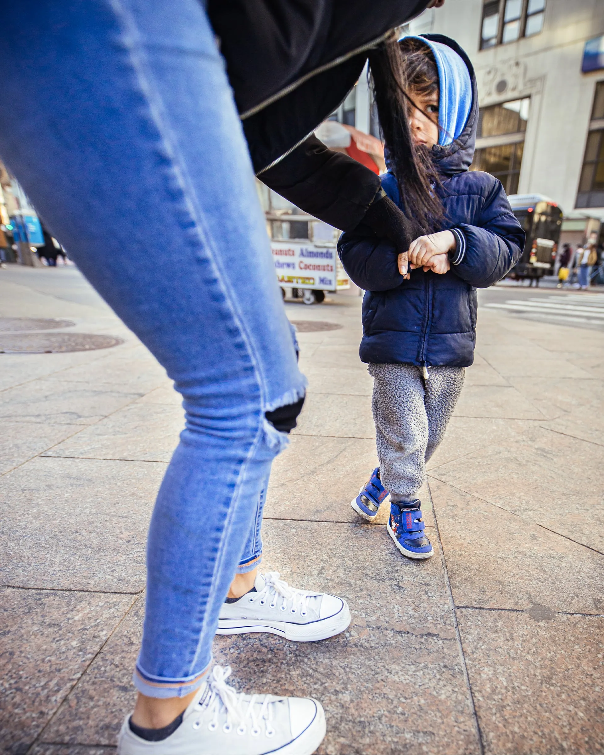 Child in a puffer coat led by the hand across a plaza
