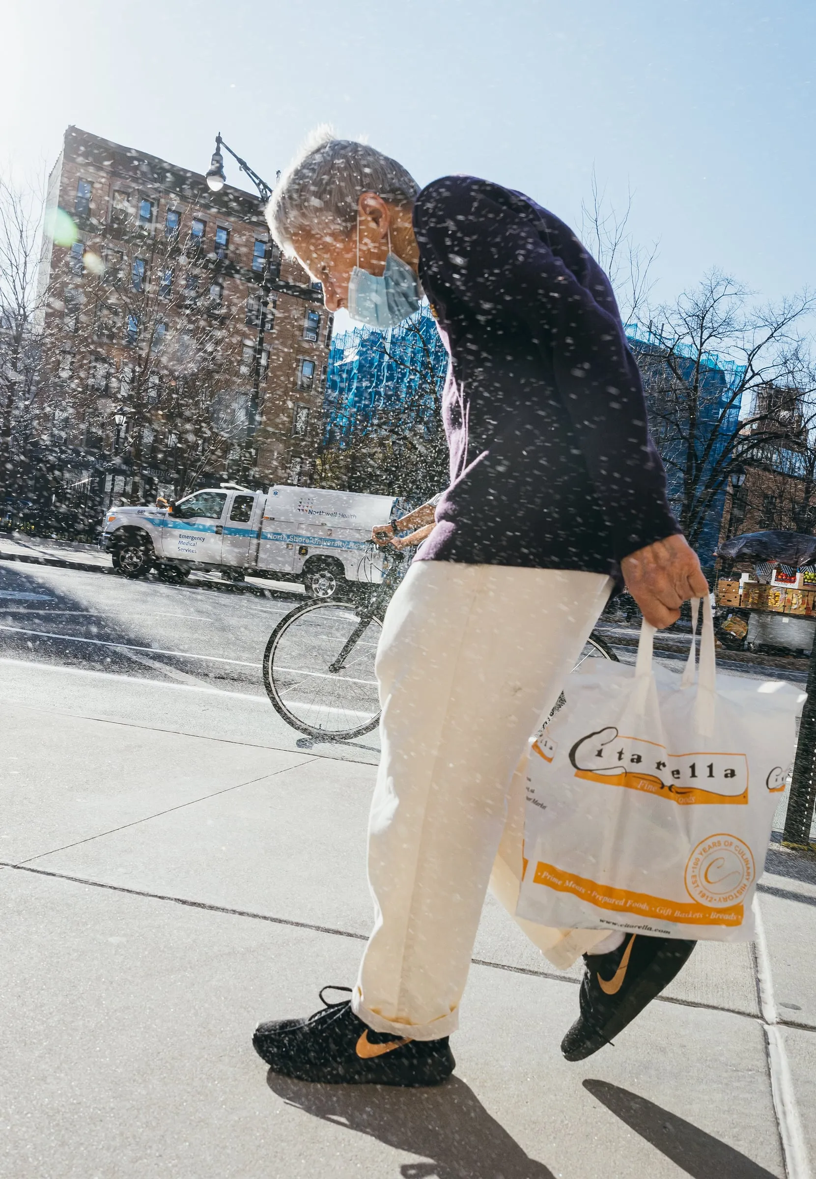Older man carrying a grocery bag through falling snow