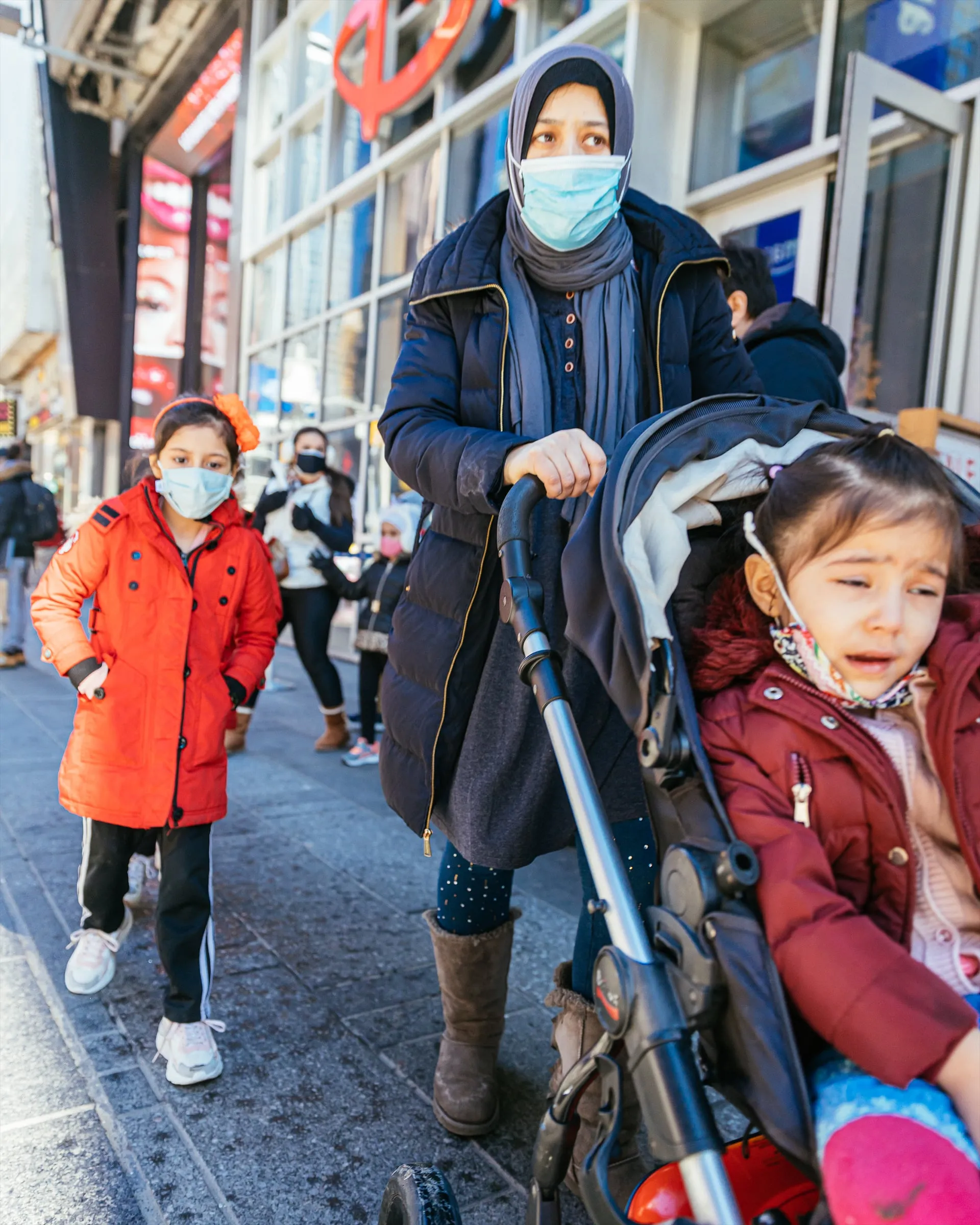 Mother pushing a stroller down a busy masked sidewalk