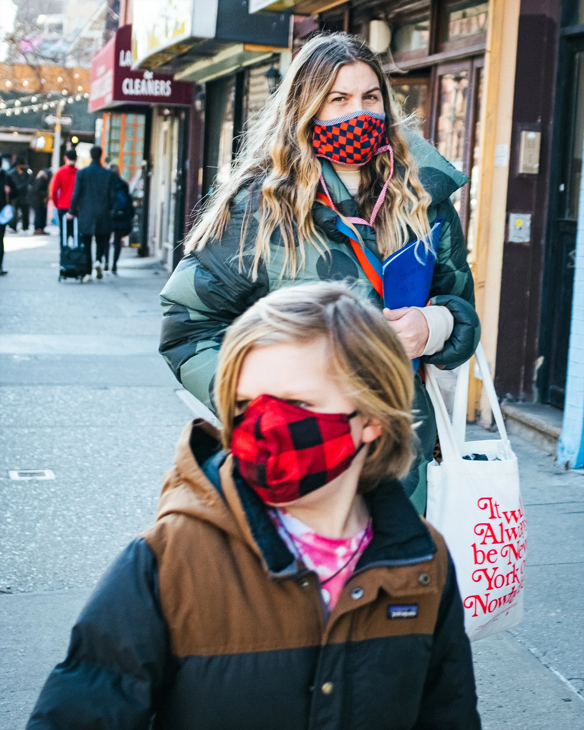 Parent and child in plaid masks walking past storefronts