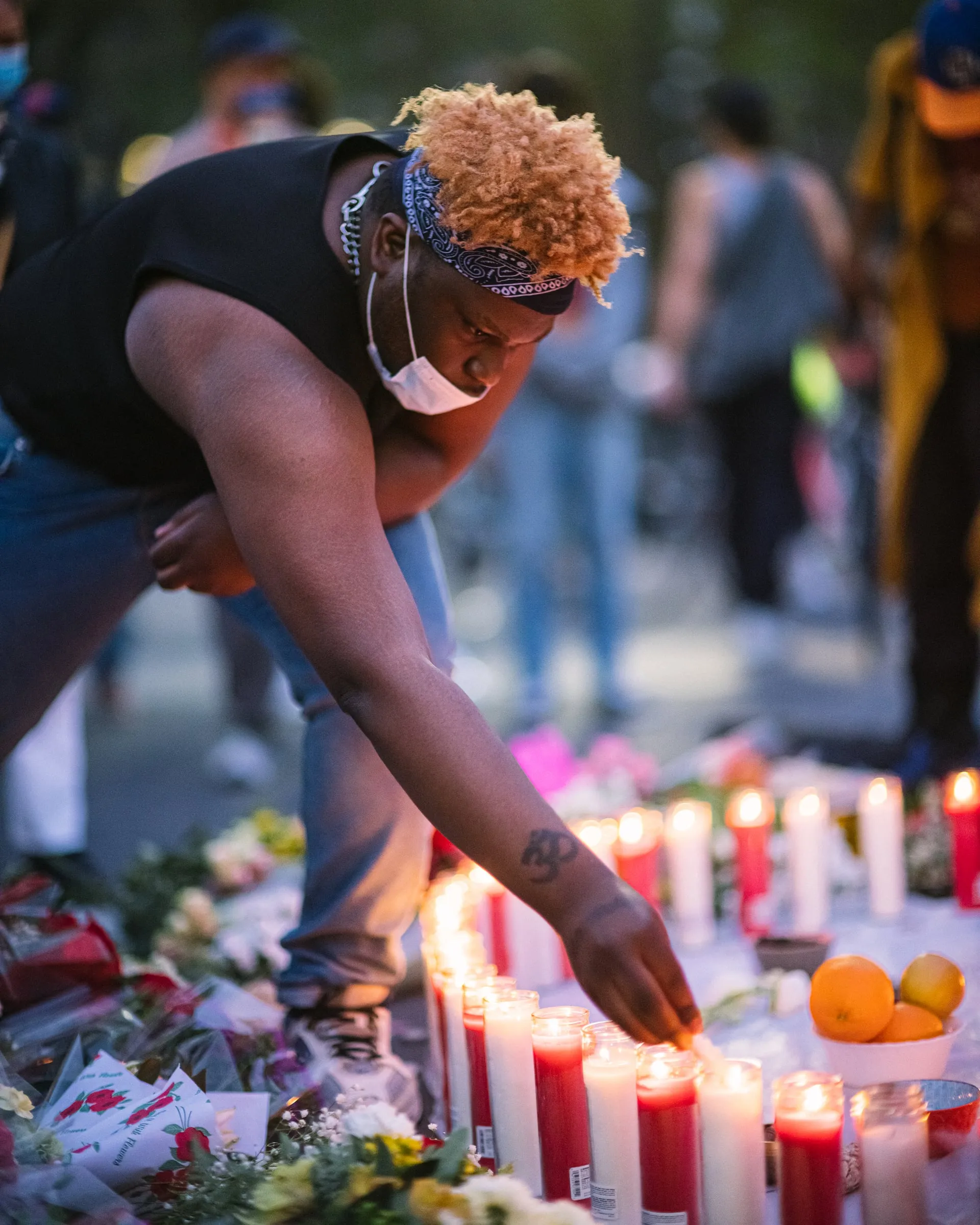 Man lighting candles at a memorial of flowers and fruit at dusk