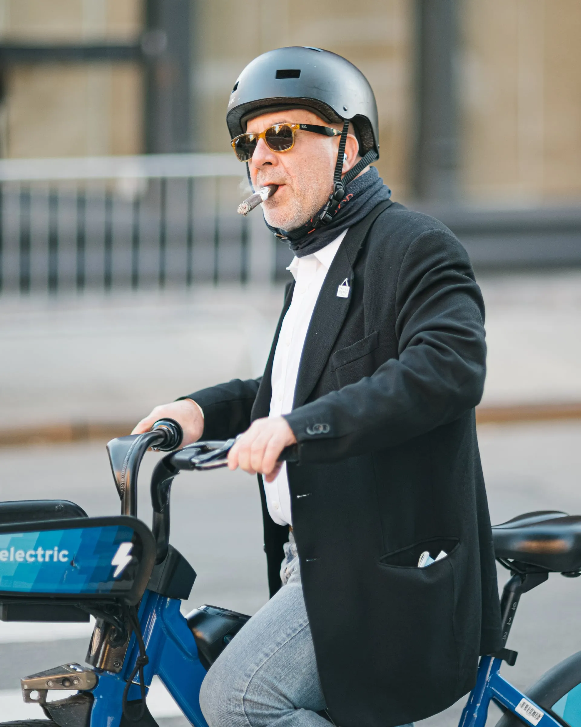 Man in a blazer riding a bike-share e-bike with a cigar